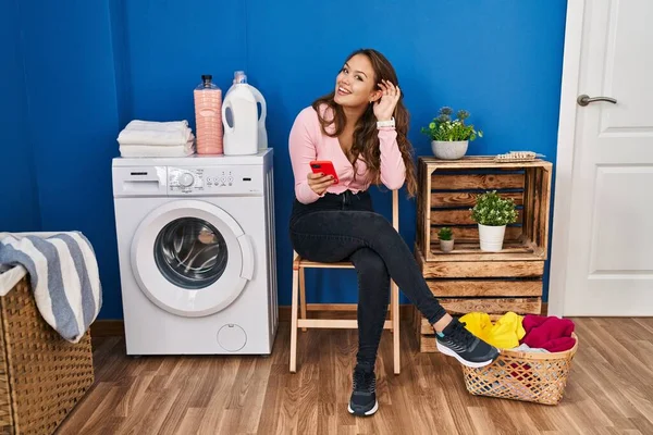 Mujer Hispana Joven Sentada Esperando Lavandería Usando Teléfono Inteligente Sonriendo —  Fotos de Stock