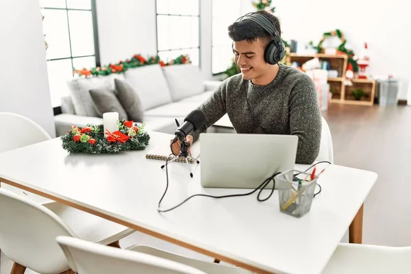 Young hispanic man radio worker working sitting by christmas tree at home