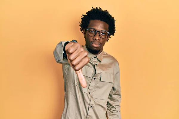 カジュアルな服と眼鏡を身に着けている若いアフリカ系アメリカ人の男性は 親指を下にジェスチャーで拒絶と否定を示す不満と怒りを見ている 悪い表現 — ストック写真