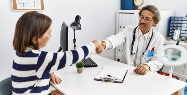 Middle age man and woman wearing doctor uniform having medical consultation shake hands at clinic