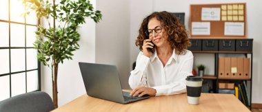 Ofiste çalışan orta yaşlı İspanyol kadın akıllı telefondan konuşuyor.