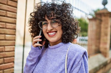 Orta Doğulu genç bir kadın gülümsüyor. Akıllı telefondan konuşuyor.