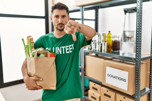 Young Hispanic Man Wearing Volunteer Shirt Holding Groceries Angry Face — Foto de Stock