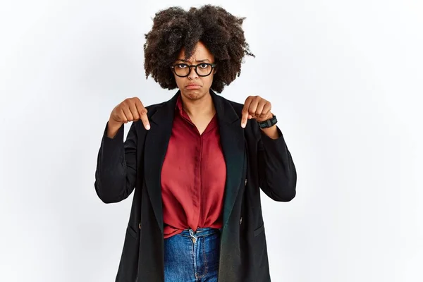 African american woman with afro hair wearing business jacket and glasses pointing down looking sad and upset, indicating direction with fingers, unhappy and depressed.