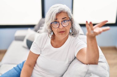 Orta yaşlı bir kadın koltukta oturmuş evde konuşuyor.