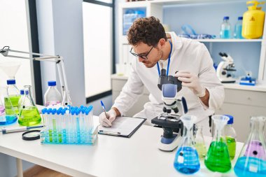 Genç İspanyol bilim adamı, laboratuarda mikroskop kullanarak belgeye yazı yazıyor.