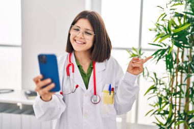 Young hispanic doctor woman working on online appointment smiling happy pointing with hand and finger to the side 