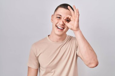 İzole edilmiş arka planda duran genç adam el hareketleriyle gülümsüyor ve mutlu yüzüyle parmaklarının arasından bakıyor.. 