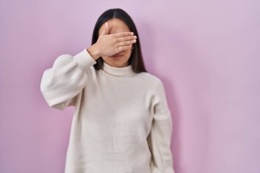 Güney Asyalı genç bir kadın pembe arka planda duruyor. Elleriyle gözlerini kapatıyor, ciddi ve üzgün görünüyor. Görme, saklama ve reddetme konsepti 