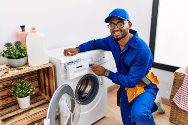 Çamaşır odasında çamaşır makinesini tamir eden teknisyen üniforması giyen genç bir Arap.