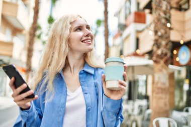 Genç sarışın kadın güneşli bir günde akıllı telefon kullanıyor.