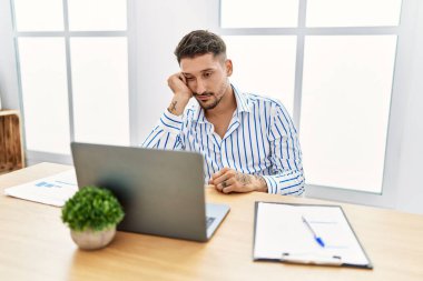 Young handsome man with beard working at the office using computer laptop thinking looking tired and bored with depression problems with crossed arms. 