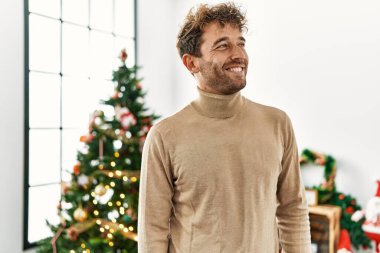 Evde Noel ağacının yanında kendinden emin gülümseyen genç İspanyol adam.