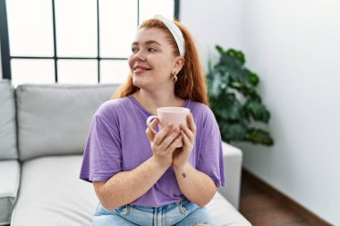 Genç, kızıl saçlı, kendine güvenen, evde kahve içen bir kadın.