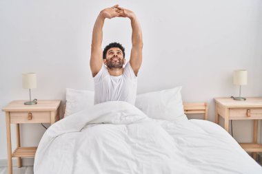 Young arab man waking up stretching arms at bedroom