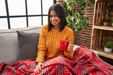 Kanepede oturup kahve içen genç İspanyol kadın kameraya seksi bir ifadeyle bakıyor, neşeli ve mutlu bir yüzle.. 