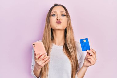 Akıllı telefon ve kredi kartı şişiren komik yüzlü genç sarışın kız. Ağzı havayla şişer, havayı yakalar.. 