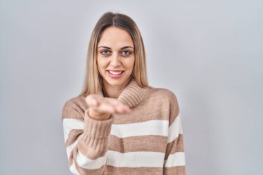 Münzevi bir arka plan üzerine balıkçı yaka kazak giyen genç sarışın kadın gülümseyerek avuç içi yardım ve kabullenme teklif ediyor.. 