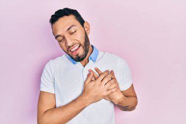 Sakallı, sıradan beyaz tişörtlü, elleri göğsünde, gözleri kapalı, yüzünde minnet ifadesi olan İspanyol bir adam. sağlık kavramı. 