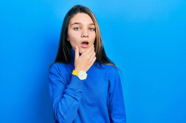 Balıkçı yaka kazak giyen genç esmer kız, elleri çenesinde olan inançsızlıktan, şaşkınlıktan ve şaşkınlıktan büyülenmiş görünüyor. 