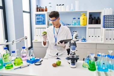 Laboratuvarda elma tutan bilim adamı üniforması giyen genç İspanyol adam.