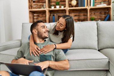 Evde dizüstü bilgisayar kullanarak mutlu gülümseyen genç Latin çift..