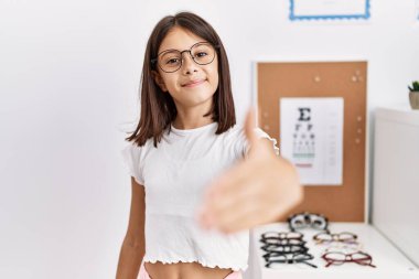 Young hispanic girl wearing glasses smiling friendly offering handshake as greeting and welcoming. successful business. 