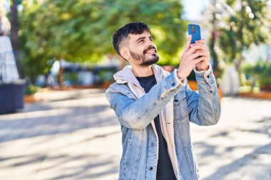 Young hispanic man smiling confident making photo by smartphone at park