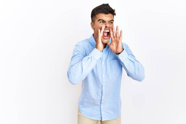 İş gömleği giyen genç İspanyol adam izole arka planda duruyor ve elleri ağzında bağırıyor. 
