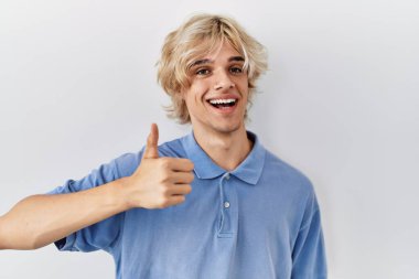 Soyutlanmış arka planda duran genç ve modern bir adam elleriyle mutlu bir jest yapıyor. Kameraya bakıp başarıyı gösteren ifade. 