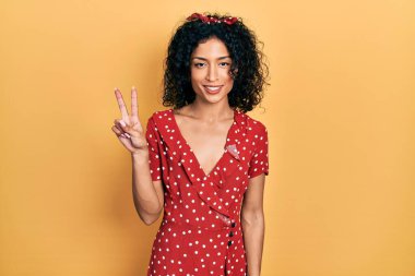 Yazlık elbise giyen genç Latin kız iki numarayı gösterip işaret ederken kendinden emin ve mutlu bir şekilde gülümsüyor.. 
