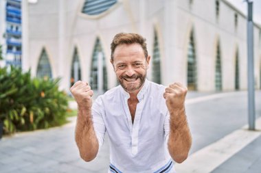 Şehirdeki orta yaşlı adam çok mutlu ve heyecanlı bir şekilde kollarını kaldırıp, gülümseyip, başarı için bağırarak kazanan bir jest yapıyor. kutlama konsepti. 