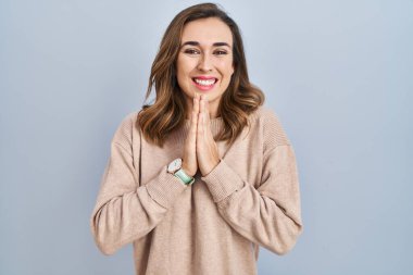 Young woman standing over isolated background praying with hands together asking for forgiveness smiling confident. 