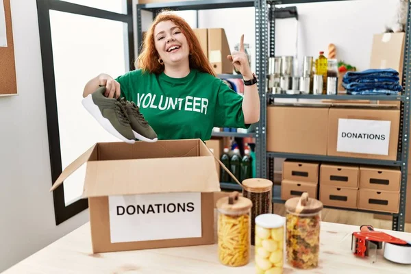 Young Redhead Woman Wearing Volunteer Shirt Holding Second Hand Sneakers — Stock Photo, Image