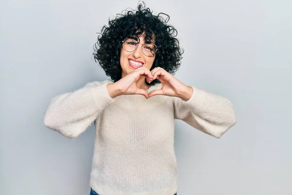 Young middle east woman wearing casual white tshirt smiling in love doing heart symbol shape with hands. romantic concept.