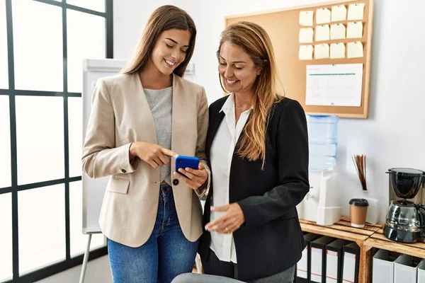 Mother and daughter business workers smiling confident using smartphone at office