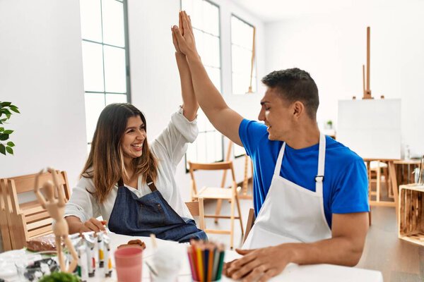 Two students smiling happy modeling clay and high five at art school.