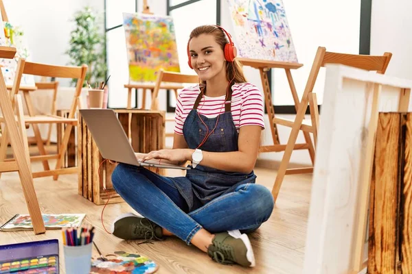 在艺术工作室使用笔记本电脑和耳机时 年轻女子自信地微笑着 — 图库照片