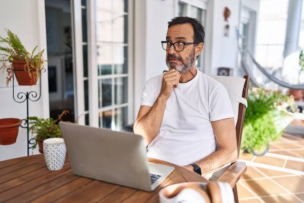 Middle age man using computer laptop at home thinking worried about a question, concerned and nervous with hand on chin