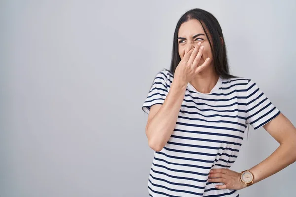 Young Brunette Woman Wearing Striped Shirt Smelling Something Stinky Disgusting — Zdjęcie stockowe