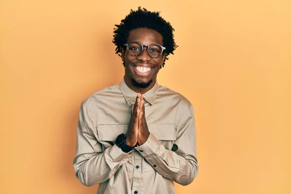 年轻的非洲裔美国人 身穿休闲装 戴着眼镜 手拉手祈祷 祈求宽恕 脸上带着自信的笑容 — 图库照片