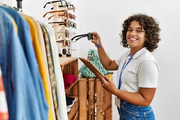 Young latin shopkeeper woman smiling happy working at clothing store.