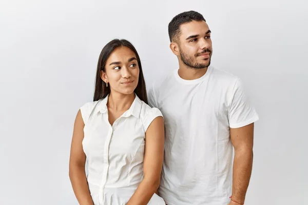 Young interracial couple standing together in love over isolated background smiling looking to the side and staring away thinking.