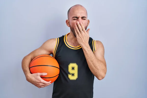 Ung Skallig Man Med Skägg Basketuniform Håller Bollen Uttråkad Gäspande — Stockfoto