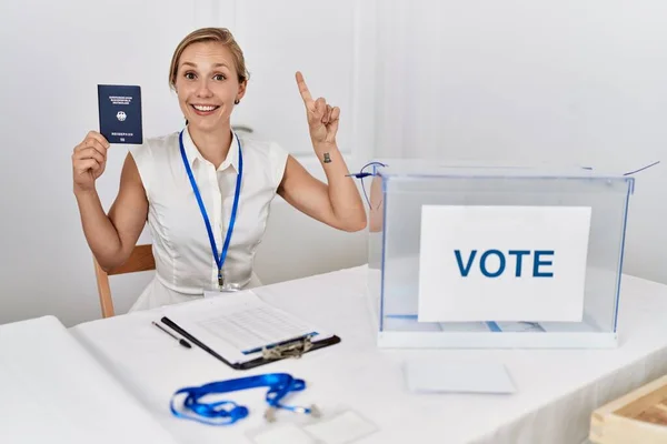 Young blonde woman at political campaign election holding germany passport surprised with an idea or question pointing finger with happy face, number one