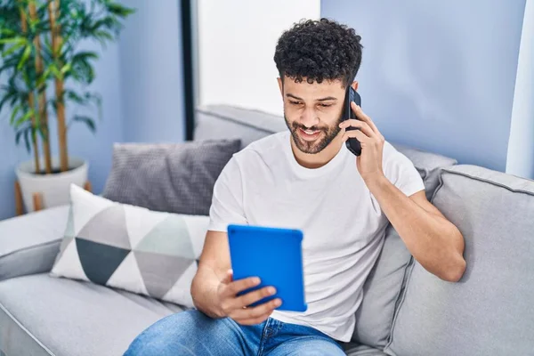 Jovem Árabe Homem Falando Smartphone Usando Touchpad Sentado Sofá Casa — Fotografia de Stock