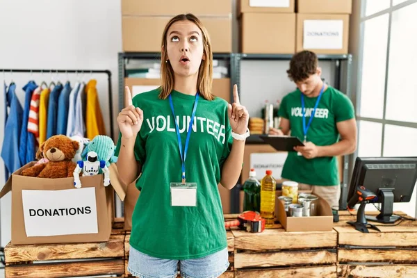 Young Blonde Girl Wearing Volunteer Shirt Donation Stand Amazed Surprised — Φωτογραφία Αρχείου