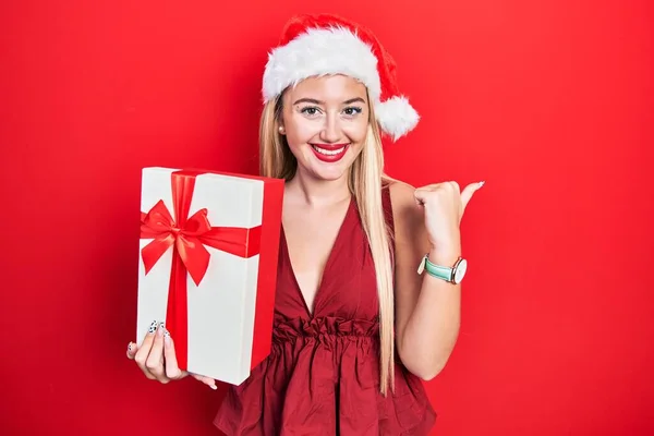 Jovem Loira Vestindo Chapéu Natal Segurando Presentes Apontando Polegar Até — Fotografia de Stock