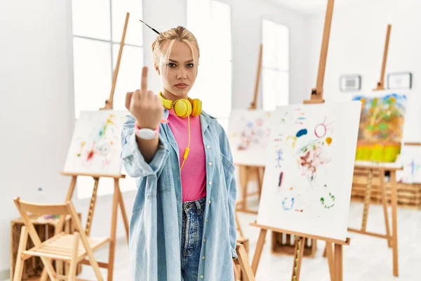 Young caucasian girl at art studio showing middle finger, impolite and rude fuck off expression