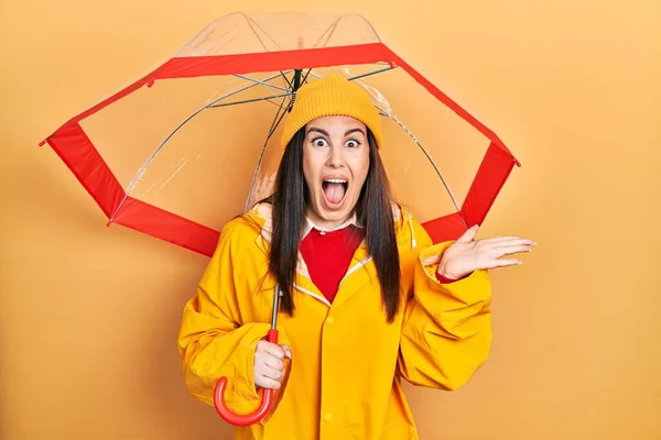 Young Hispanic Woman Wearing Yellow Raincoat Holding Umbrella Celebrating Victory — Foto Stock